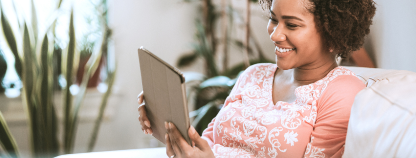 A smiling Black women sitting down reading on a tablet computer
