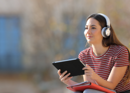 woman sitting down with headphones on and holding a tablet