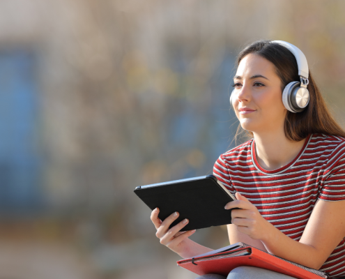woman sitting down with headphones on and holding a tablet