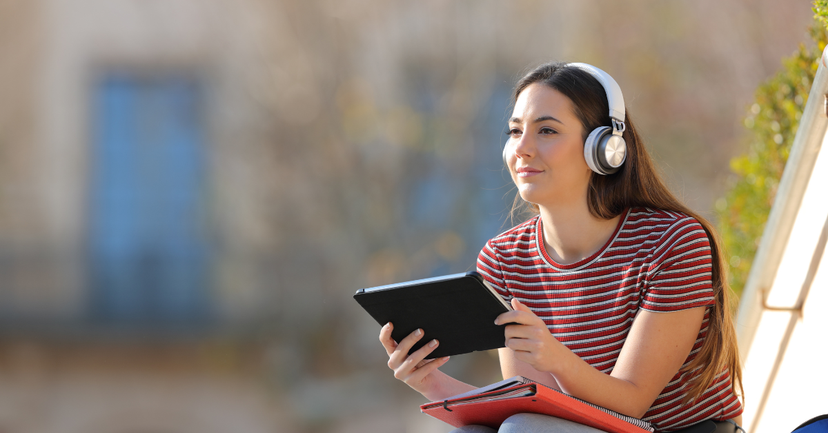 woman sitting down with headphones on and holding a tablet