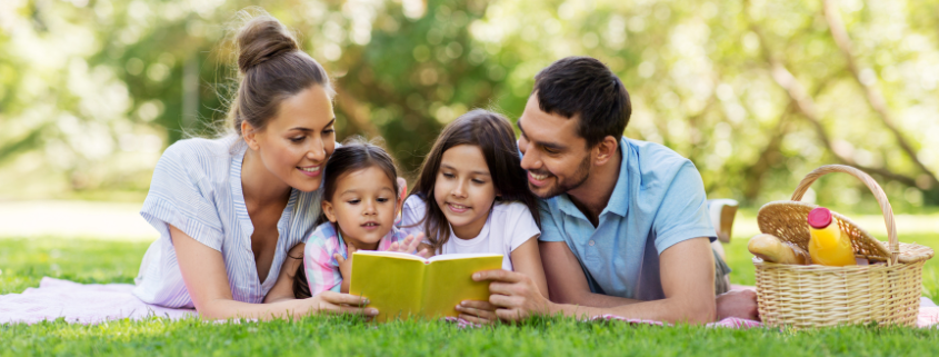 Two parents with two children laying in the grass reading a book together