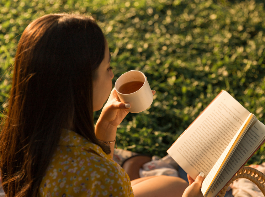 Woman holding a cup of coffee in her left hand and an open book in her right hand reading
