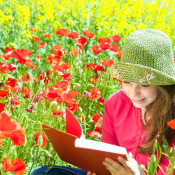 Young girl wearing a green hat reading a book in a flower field