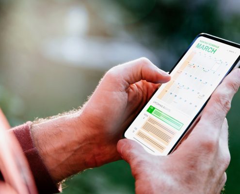 Photograph of adult hands holding a smartphone with a calendar app on it