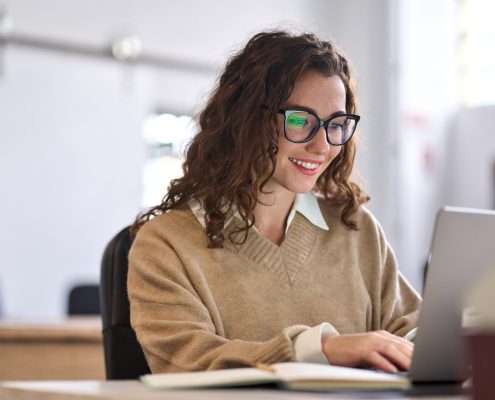 Young happy woman sitting at desk using laptop.